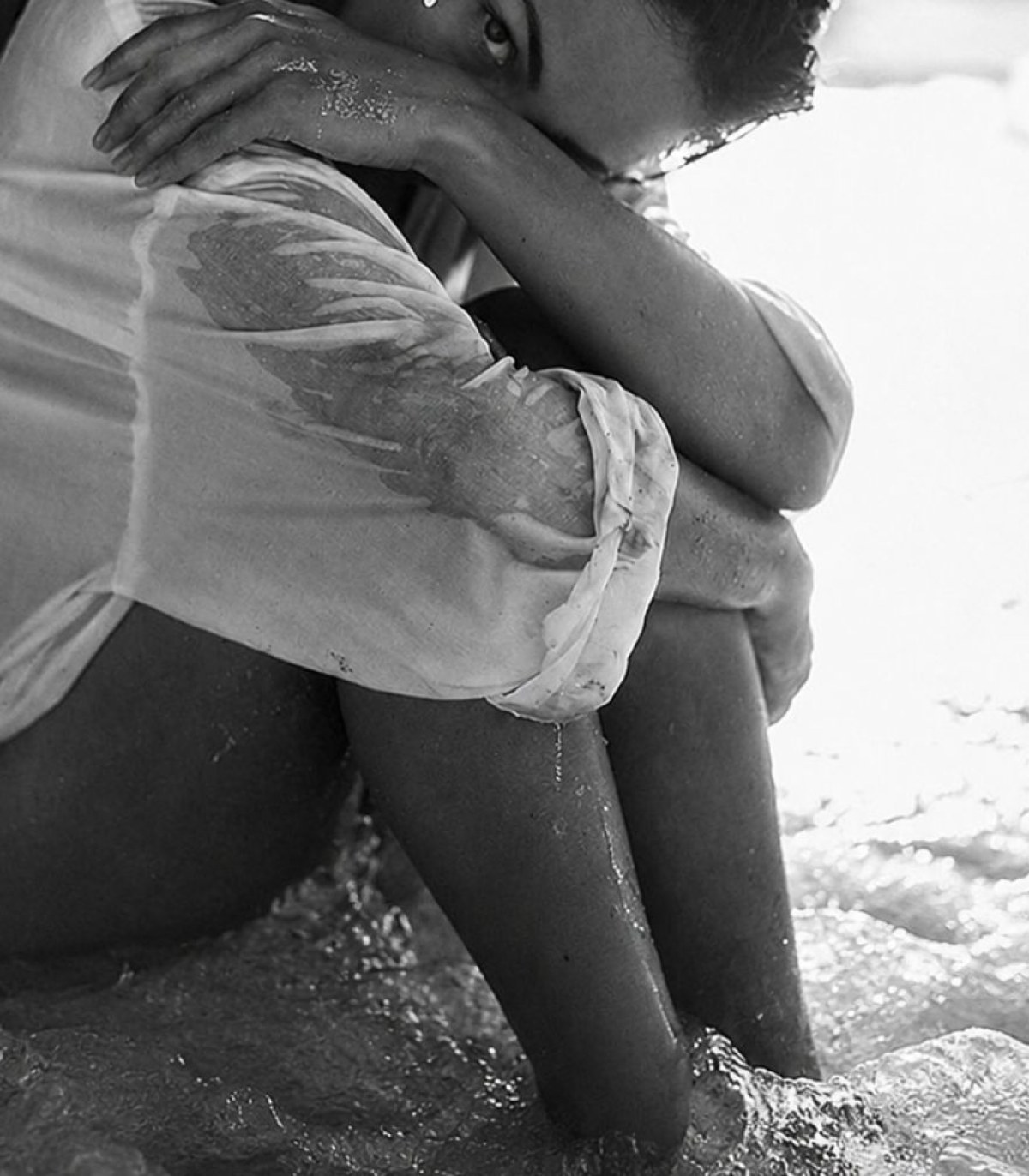 A person sitting at the water's edge with their arms wrapped around their knees