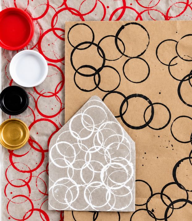 Circles stamped in red, black and white ink across kraft paper and tissue, beside open pots of red, white, black and gold paint
